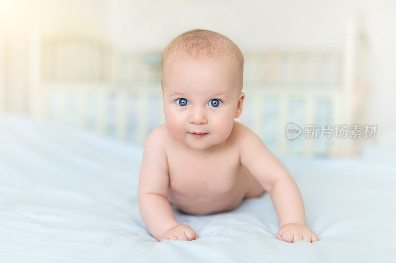 可爱可爱的5个月大的白人小男婴躺在育婴室的床上，开心地玩耍和微笑。快乐健康的新生儿概念。有趣的幼儿特写肖像