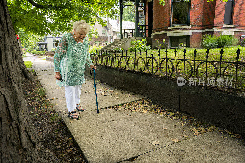 拄着拐杖走在不平的人行道上的老年人