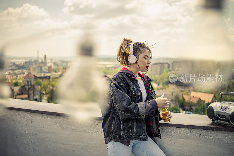 一个年轻的复古风格的女孩在楼顶听音乐-他在楼顶听音乐，享受自由，喝酒