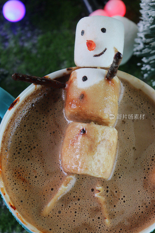 棉花糖雪人坐在绿松石蓝色杯的热巧克力泡沫，以绿松石蓝色舌头和槽效果背景，仙女灯和模型圣诞树，高架视图