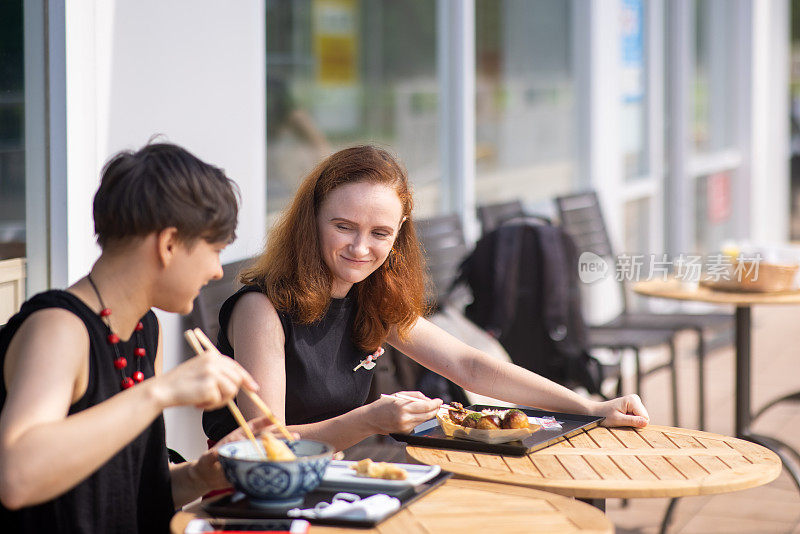 两个白人妇女在户外咖啡厅吃乌冬和章鱼烧午餐