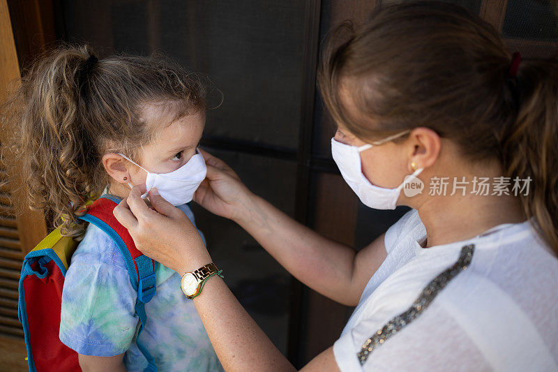 2019冠状病毒病期间母女佩戴防护口罩准备上学。新常态