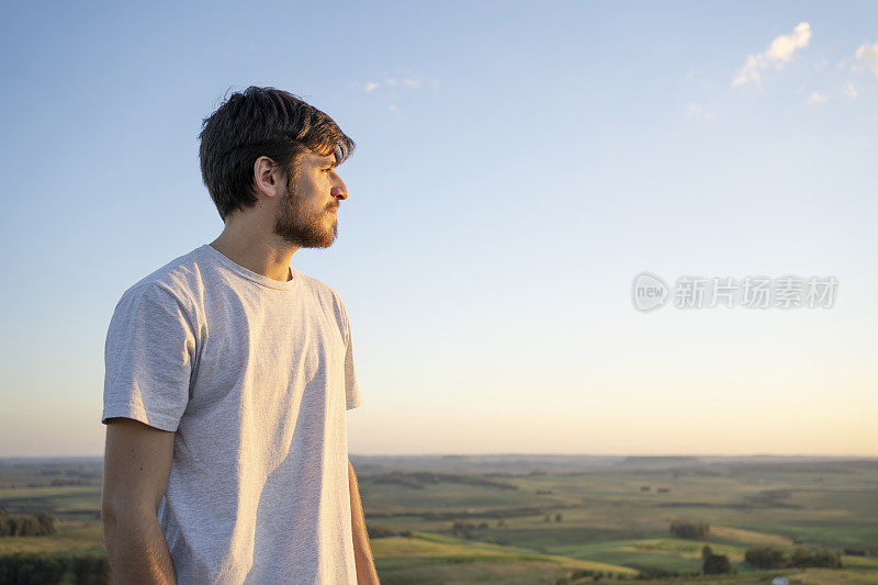 夕阳西下时，一个年轻人站在山顶眺望地平线。想象未来。