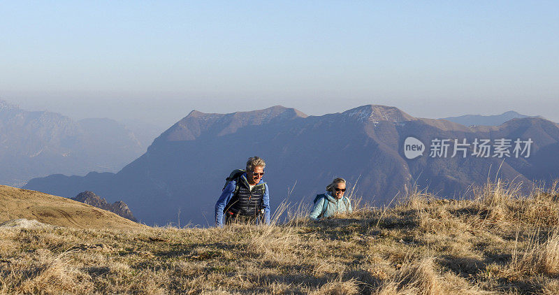 成年夫妇沿着长满青草的山脊徒步旅行