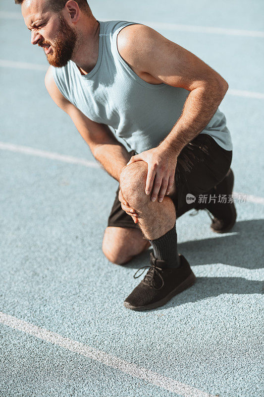 男运动员在跑道上跑步时膝盖受伤，蜷缩疼痛