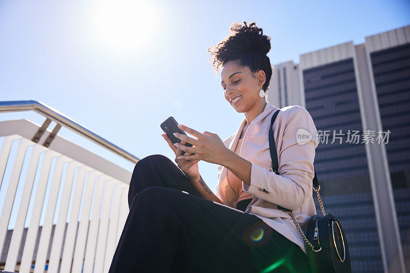 年轻的女商人坐在城市的台阶上，面带微笑地用手机发短信