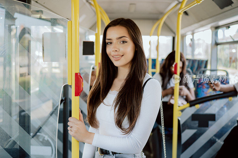 一个有吸引力的学生花了她的早上在公共汽车上去大学，一个年轻的美丽的女人使用公共交通站在门口等车停在公共汽车站