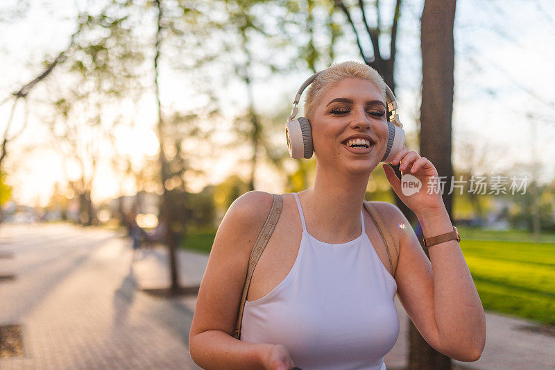 微笑着的年轻女子，金色短发，听着音乐，穿过公园