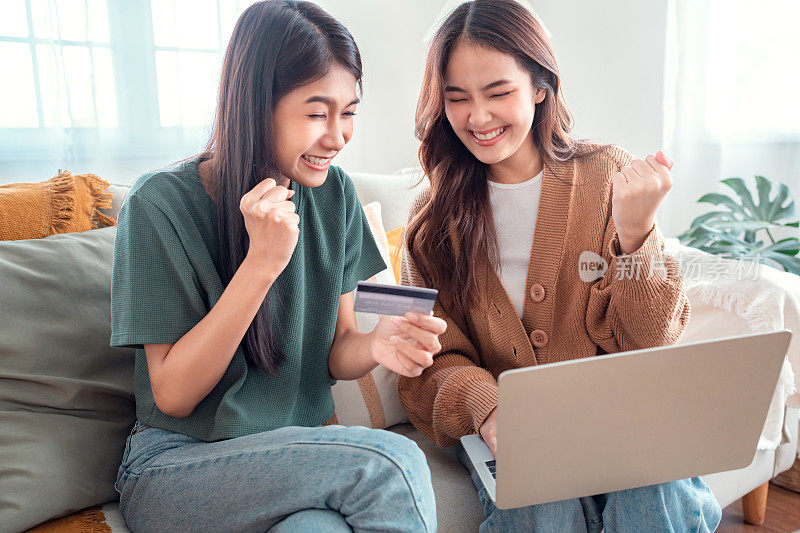 两个快乐的室友一起用信用卡和笔记本电脑坐在家里的沙发上网购。