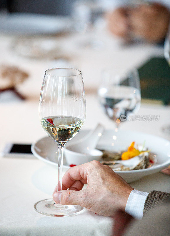 晚宴时在餐厅的餐桌上端着盛着白葡萄酒的酒杯