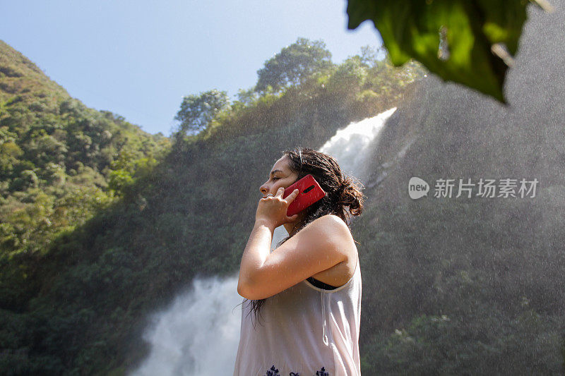 快乐的女人享受一个夏天的瀑布附近打电话