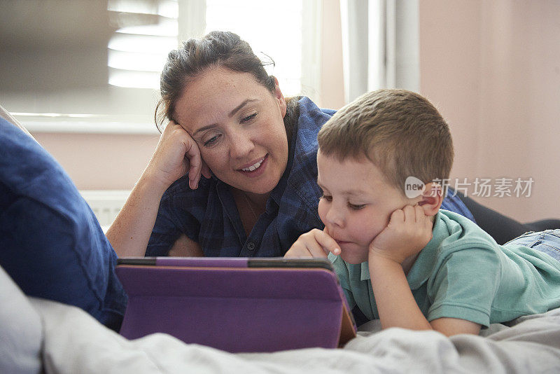 母亲和儿子躺在床上用数码平板电脑