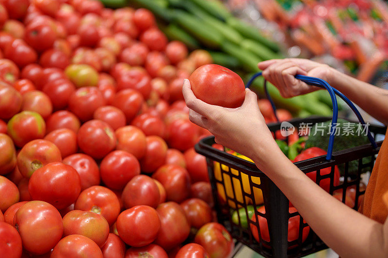 一名年轻女子提着购物篮在杂货店购买新鲜的有机水果和蔬菜