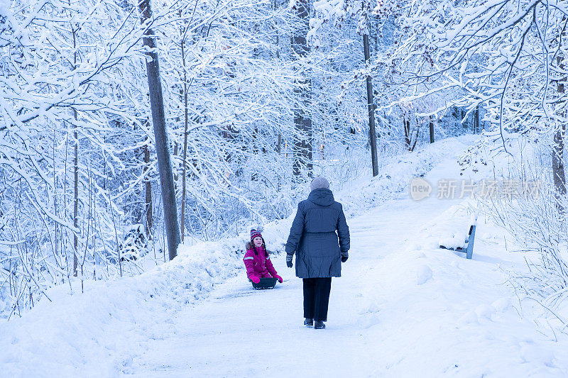 一位77岁的老妇人和一个7岁的女孩。冬天走在雪路上。祖母带着孩子坐雪橇。