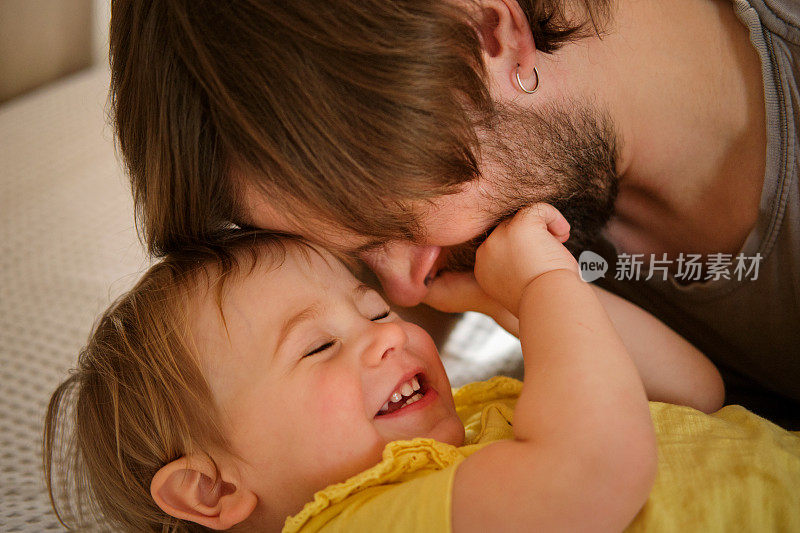 快乐的父亲和女儿，小女孩。一岁的宝宝笑着，笑着，抬头看着爸爸。男人向孩子示爱。坦诚的真实情感。胡子爸爸和小孩。真实的家庭生活方式。
