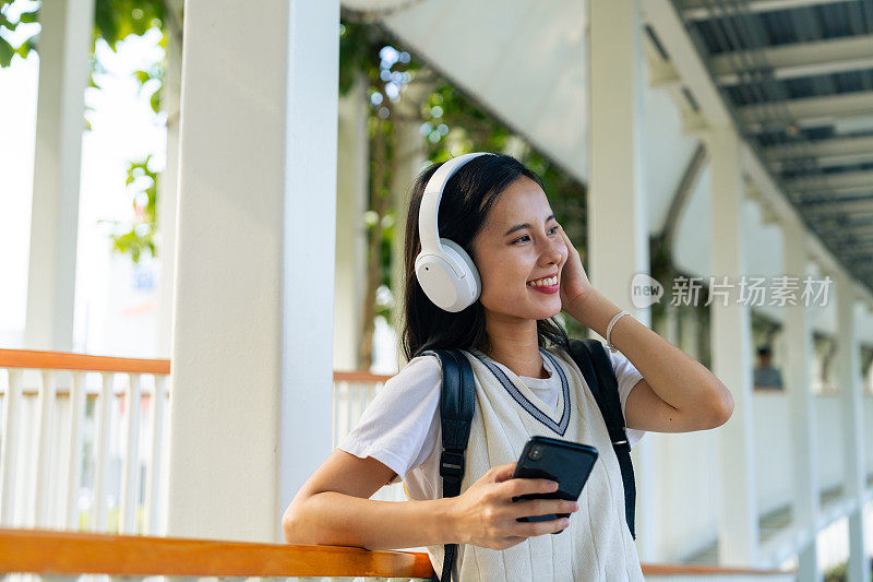 微笑的女人用智能手机和耳机拥抱大自然的旋律