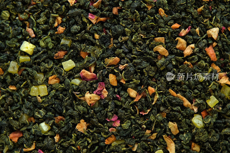 散叶芒果菠萝水果茶壁纸。混合红茶和绿茶干茶叶。特写，微距。前视图。纹理。干茶在旋转。摘要食品和饮料的背景。完整的框架。