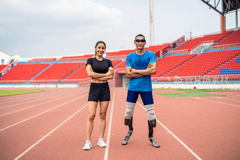 亚洲残疾人运动员和教练站在体育场的肖像。迷人的截肢男跑步者和年轻的女运动员在为残奥会比赛练习后微笑着看着镜头。