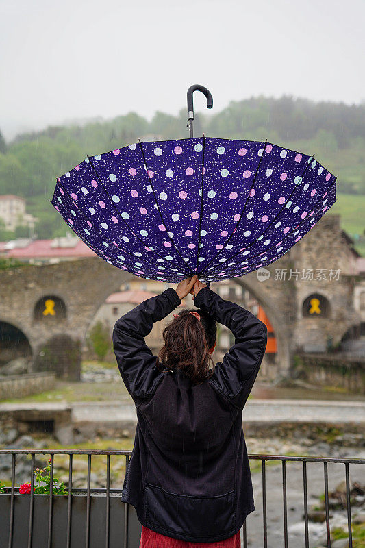 冬天，滑稽的女游客在校园拿着一把倒扣的伞。雨天的天气。冬天的生活方式