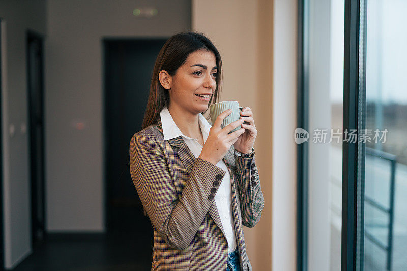 照片中，一位年轻貌美的女商人端着一杯咖啡站着