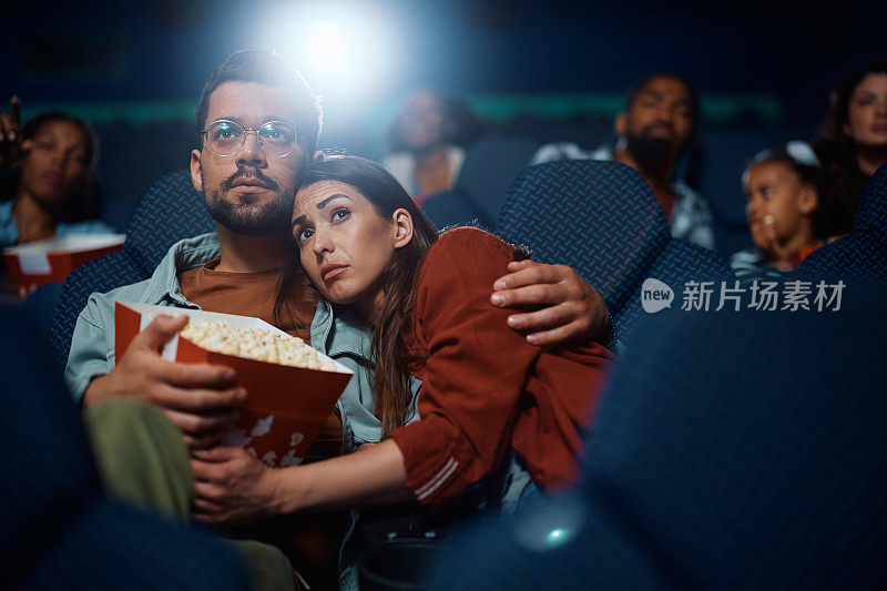 在电影院看悬疑电影的年轻情侣拥抱在一起。