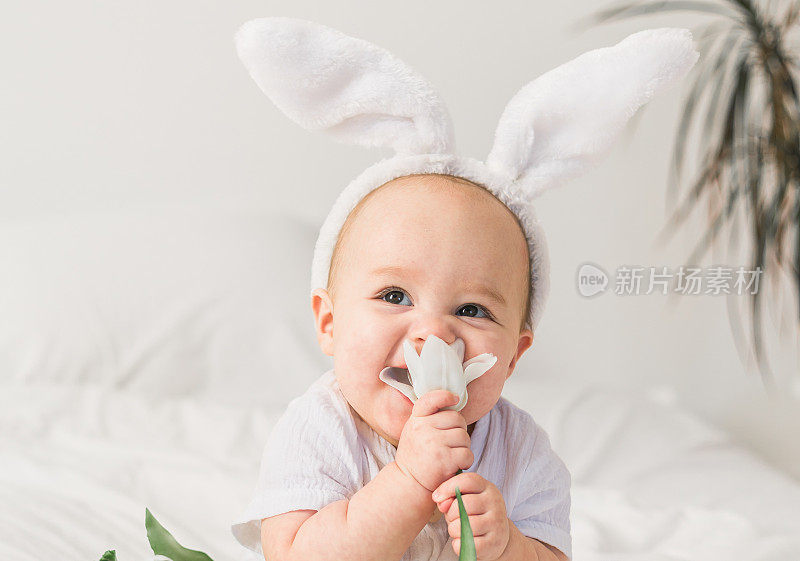 可爱的宝宝头上戴着兔子耳朵，家里的床上放着郁金香。复活节和春天时间的概念