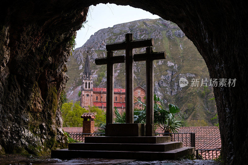 一个十字架在一个山洞里很显眼，背景是一座山。崎岖的地形增加了这一景色的神秘感