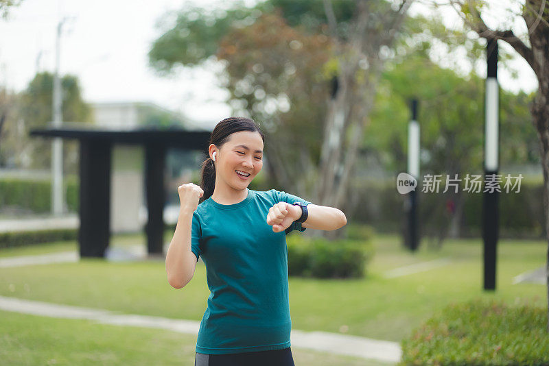 戴着耳机看着智能手表的亚洲女性对锻炼目标很满意。