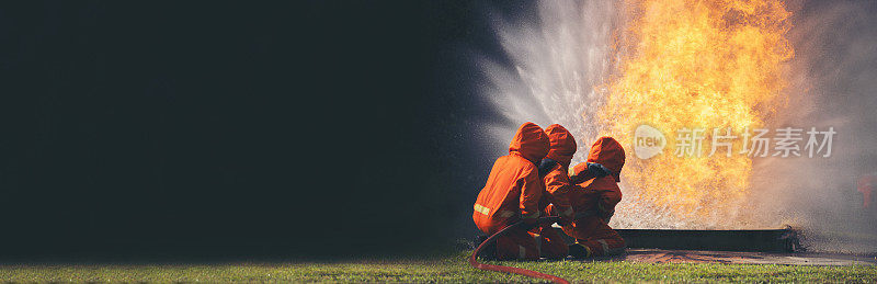 消防员灭火器救援训练。消防队员使用消防水带与火焰搏斗，化学水泡沫喷雾机。消防队员戴安全帽，穿安全防护服