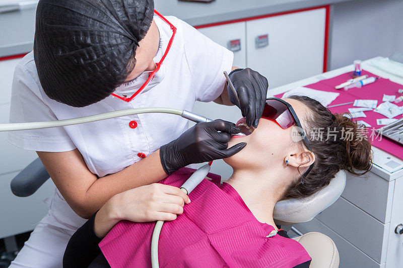 牙医在牙科诊所检查一位年轻女病人的牙齿。牙科的概念。牙科诊所里的牙医和病人。