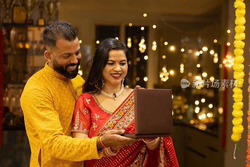 年轻的印度丈夫在排灯节或结婚纪念日送给妻子珍贵的珠宝礼物。丈夫和妻子在节日场合穿着传统服装。