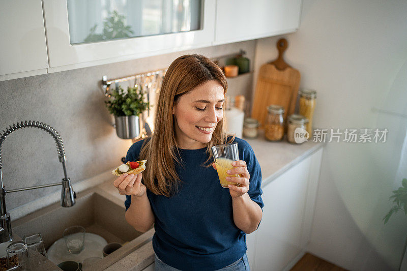 年轻女子在厨房吃烤面包当早餐，享受着烹饪的乐趣