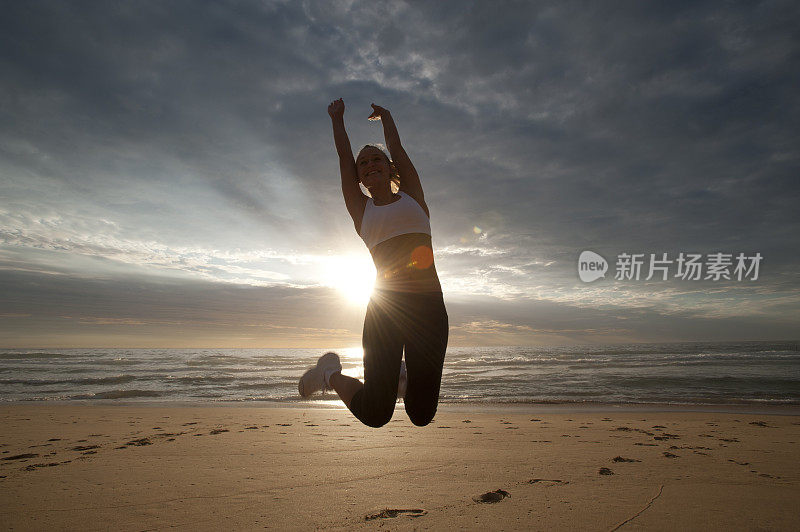 一个在海滩上跳着的女人，身后是太阳。