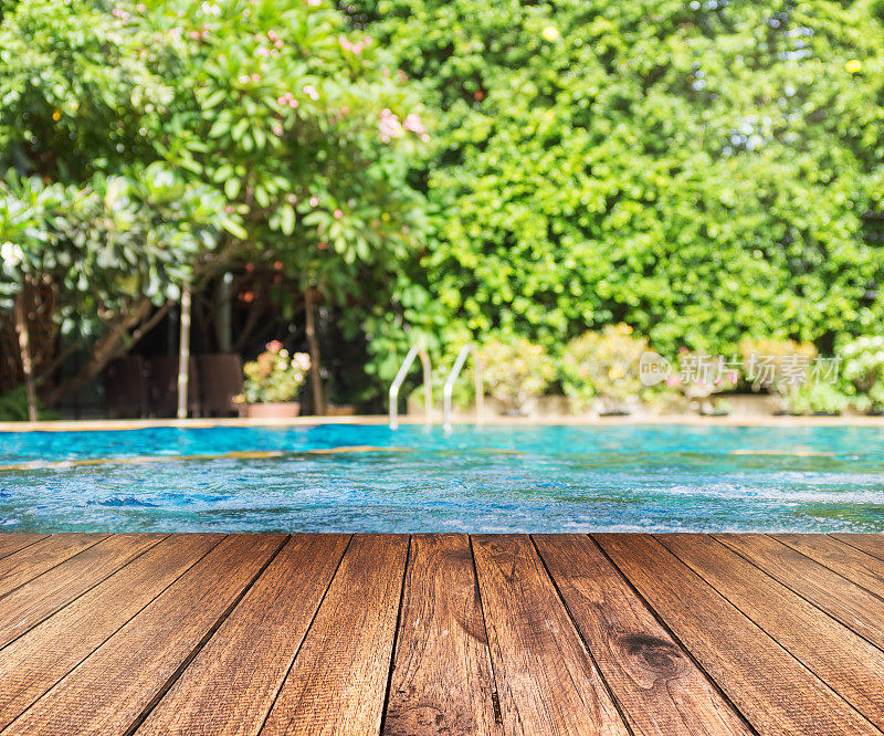 木地板靠着游泳池，绿树环绕