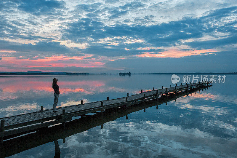 女人站在湖边码头观看雄伟的日落云景