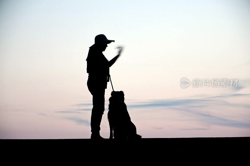 成熟的西班牙妇女和牧羊犬剪影日落