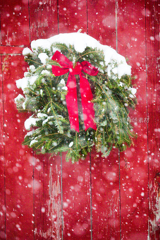 红色的谷仓门与圣诞花环在飘落的雪