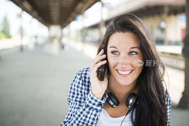 年轻快乐的女人在火车站拿着智能手机