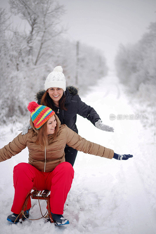 两个可爱的女孩骑着雪橇，玩得很开心