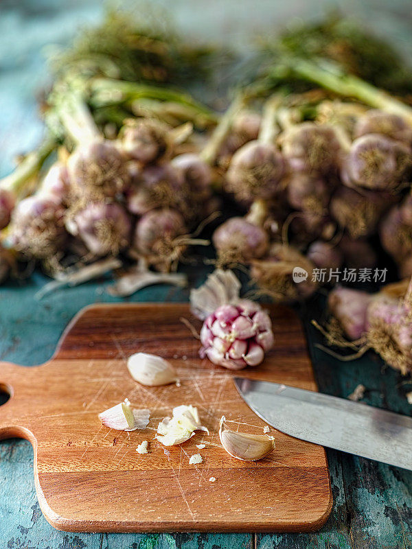 新鲜的大蒜被压碎准备烹饪在一个木砧板上，在一个破旧的绿松石蓝色木制桌子的背景。