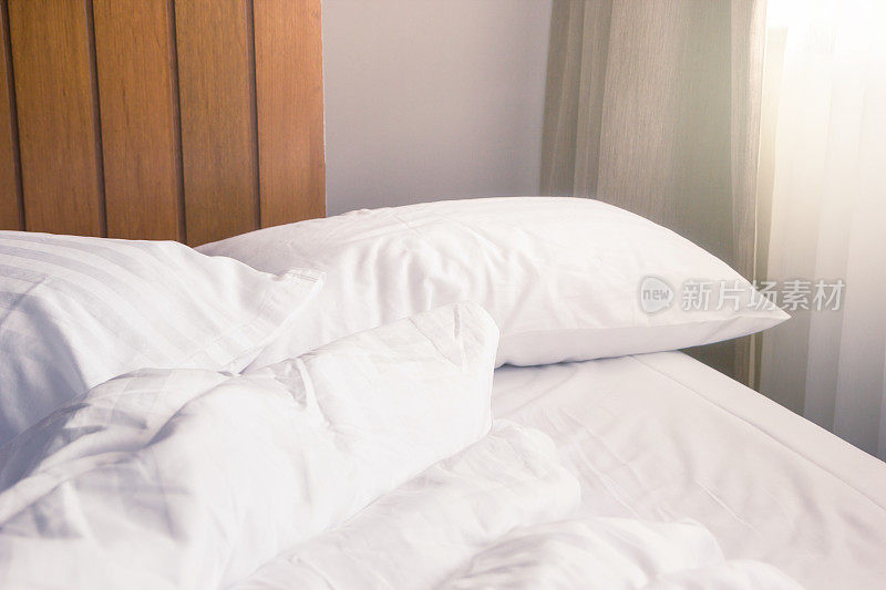 白色的枕头和褶皱的毯子凌乱地放在床上，卧室的左上方有灯光，从漫长的冬夜中入睡。