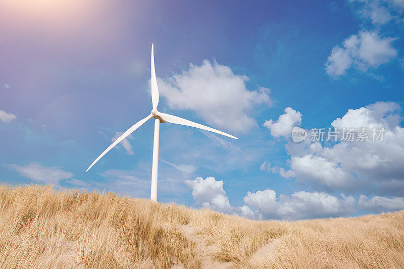 夏日蓝天下，沙丘后面的风力涡轮机覆盖着马兰草