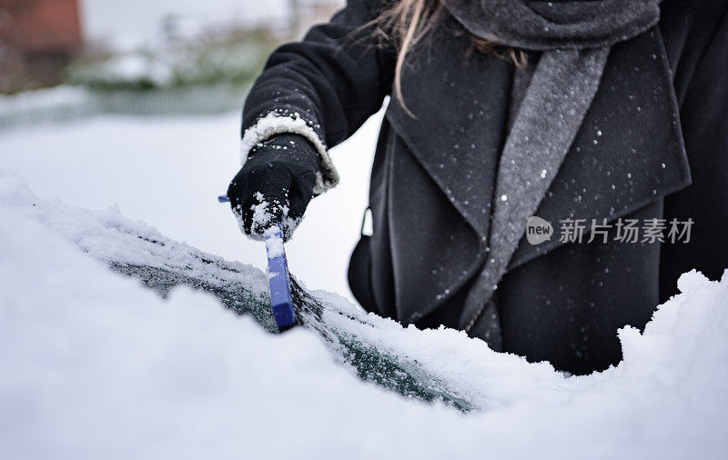 冬天即将来临。女人在冰冷的天气里，车被雪覆盖着。