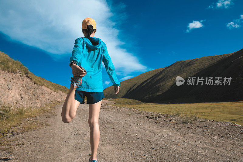 年轻的健身女子跑步伸展腿在山间小径