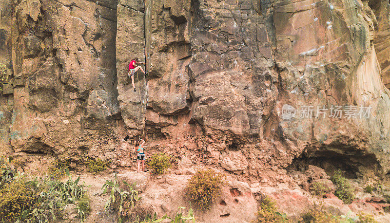 运动的人开始攀登一个峡谷的岩壁-登山者在一个岩石的地点户外训练-旅行，肾上腺素和极限运动概念-主要集中在他-未经过滤的照片