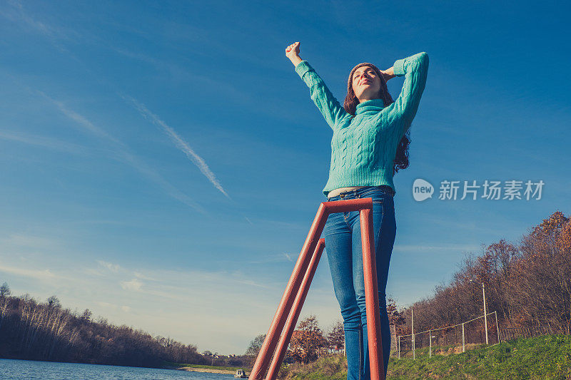 年轻女子躺在湖边的码头上，披着毯子，看日落