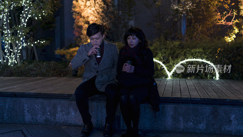 一对年轻夫妇晚上坐在城市公园的长椅上