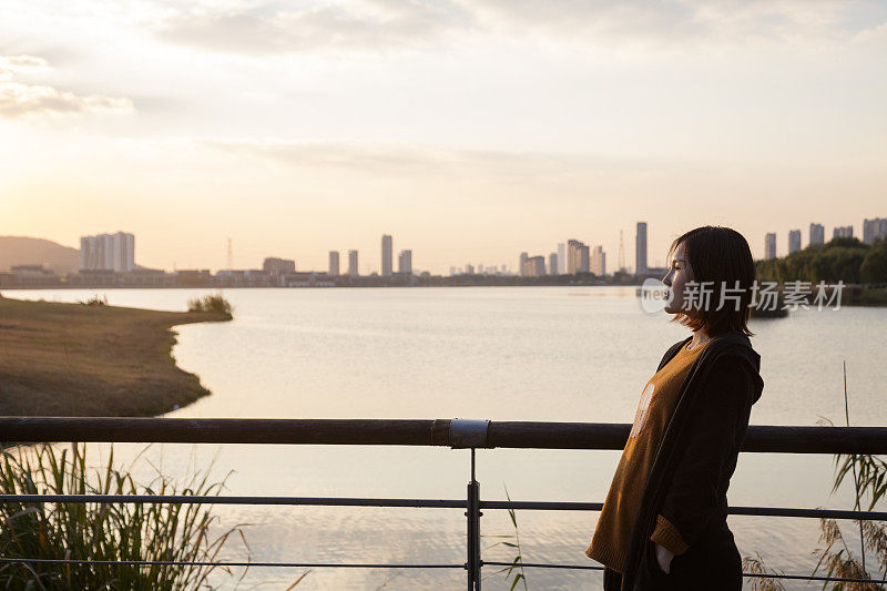 年轻女子在公园人行桥上欣赏美丽的日落风景