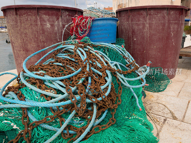 一个绿色的渔网，生锈的链条和大桶的特写