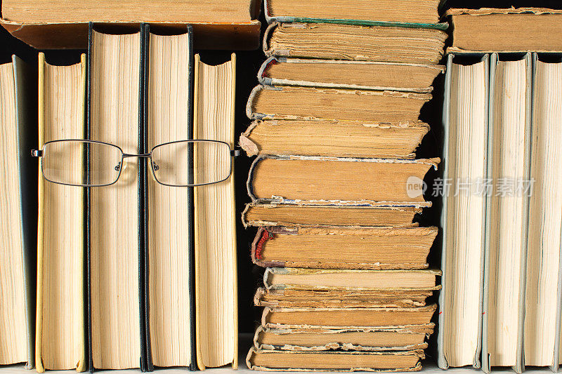 书架上有几本仿人的书，从眼镜里拿着一堆破旧的旧书。阅读的概念。